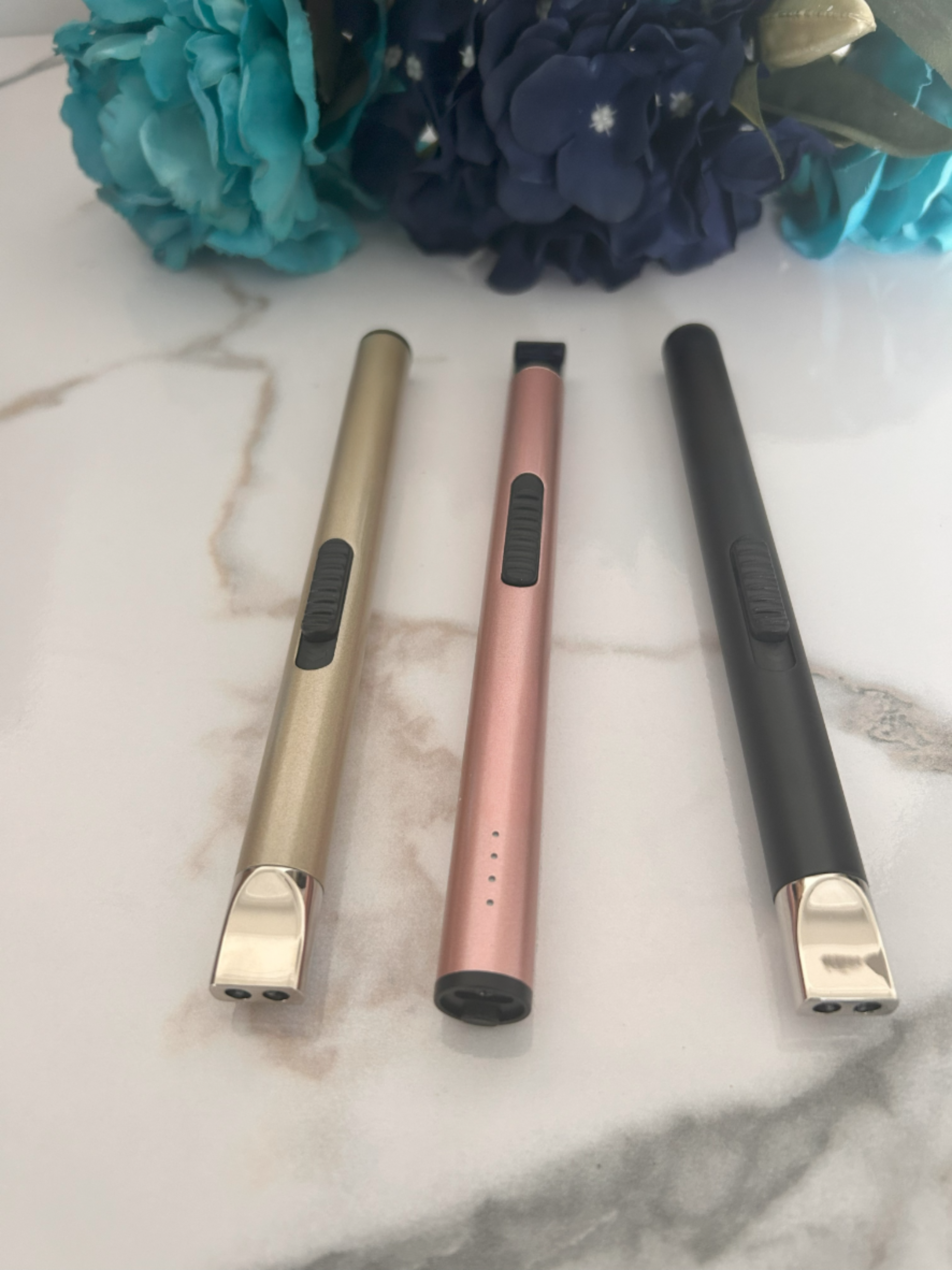 Three electronic devices in gold, rose gold, and black on a marble surface with flowers in the background.