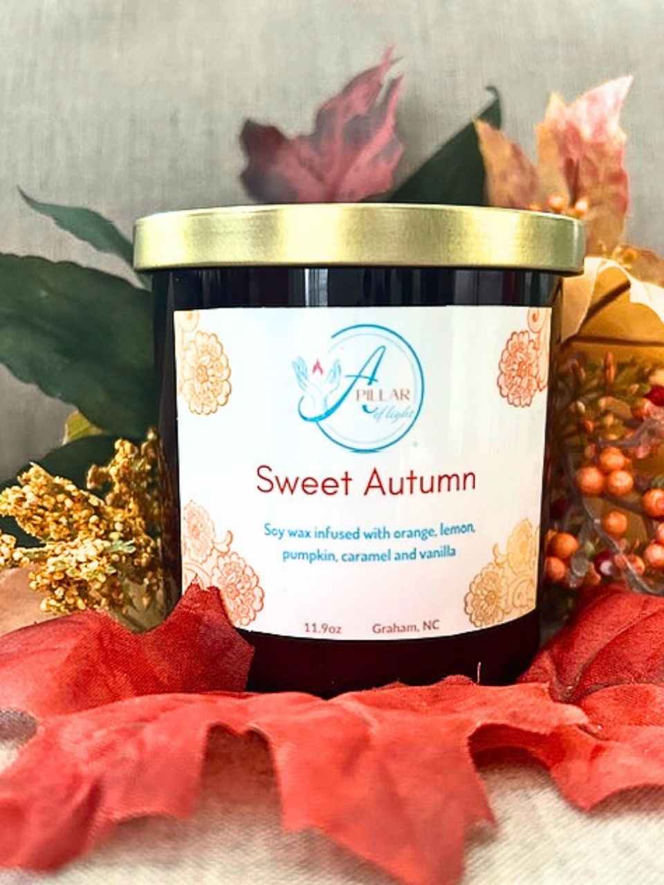 Jar of 'Sweet Autumn' candle with decorative fall elements in the background
